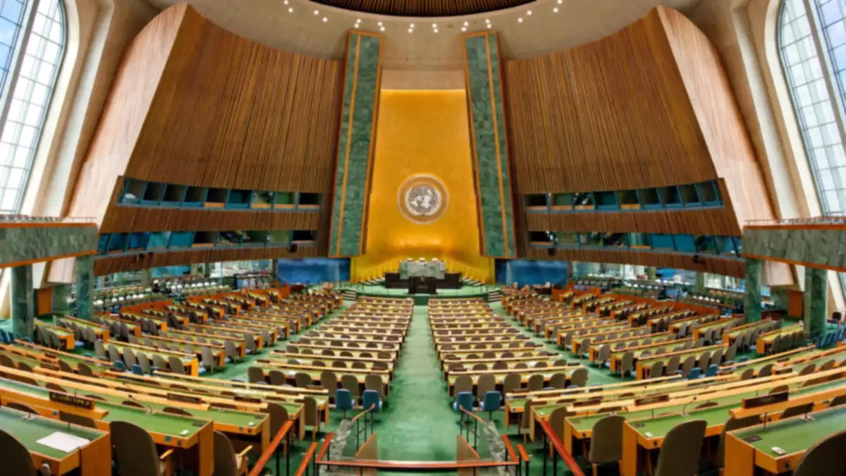 Interior of the United Nations General Assembly hall in New York with rows of delegate desks and the UN emblem